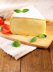 Tasty Camembert cheese with tomato and basil, on wooden table