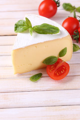 Tasty Camembert cheese with basil and tomatoes, on wooden table