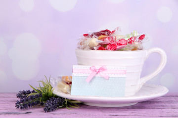 Tasty candies in mug with flowers and card