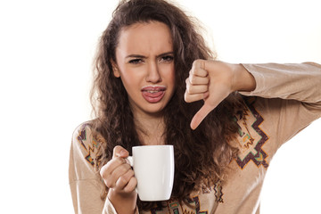 disgusted young girl with a cup of milk shows thumbs down