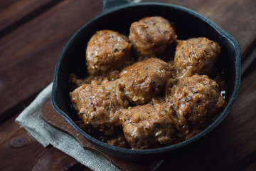 Cast-iron frying pan with meatballs, rustic wooden background