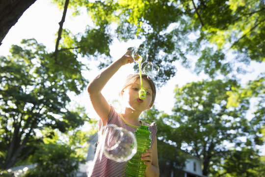 A Young Girl Blowing Bubbles In The Air Under The Branches Of A Large Tree. 