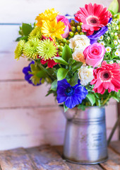 Colorful bouquet of spring flowers in vintage vase on rustic woo