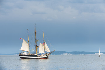 Fototapeta na wymiar Tall ship on blue water against stormy clouds. Horizontal