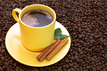 Yellow cup of coffee with cinnamon and green leaves