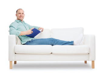 smiling man lying on sofa with book