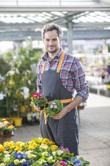 gardener holding two potted plants in a garden center