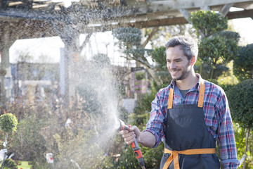 gardener watering potted trees in a garden center