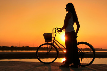 Silhouetted woman with bicycle at Mekong river waterfront at sun