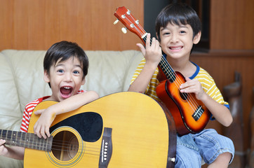 Naklejka premium little sibling boy playing guitar and ukulele happy face