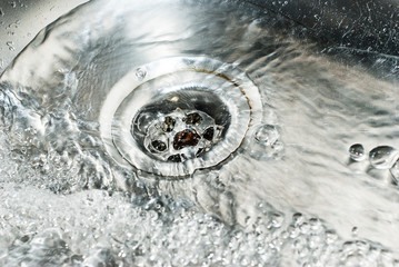 Stainless steel sink plug hole close up with water - Powered by Adobe