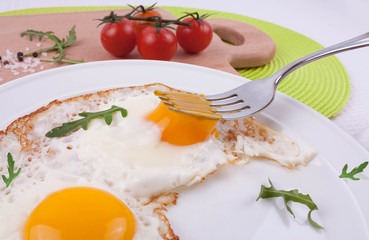 Fried eggs with arugula leaves and cherry tomatoes