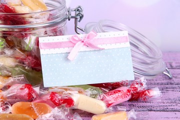 Tasty candies in jar with card on table on bright background
