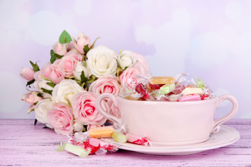Obraz na płótnie Canvas Smaczne cukierki w misce z kwiatami na stole na jasnym