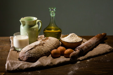 Obraz na płótnie Canvas Still life photo of bread and flour with milk and eggs at the wo