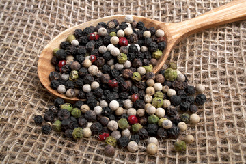 Colored pepper in wooden spoon, on burlap background