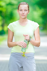 Woman drinking cold mineral water from a bottle after fitness ex