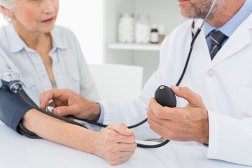 Mid section of doctor taking blood pressure of his patient - Powered by Adobe