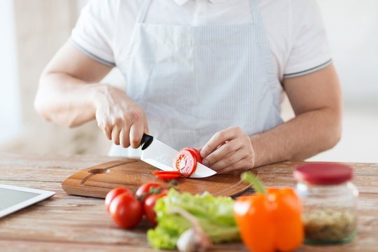 male hand cutting tomato on board with knife