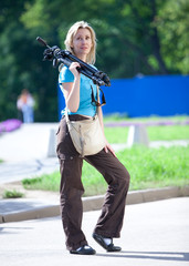 The young woman in park with a tripod on a shoulder..