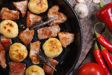New potatoes and roasted pork in a pan. Vegetables on the table.