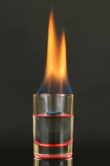Glass with burning alcohol on black background