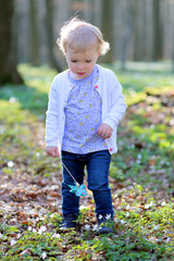 Cute toddler girl playing in spring forest holding pinwheel toy