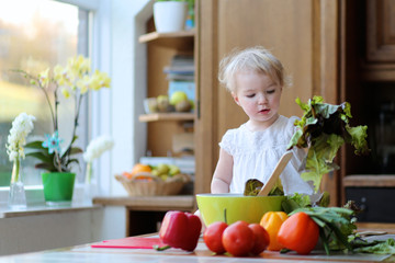 Funny toddler girl mixing vegetables in the bowl preparing salad