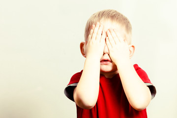 Happy childhood. Blond boy child kid covering face with hands