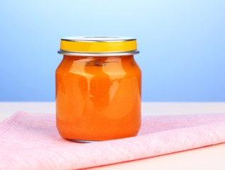 Jar of baby puree on napkin on blue background