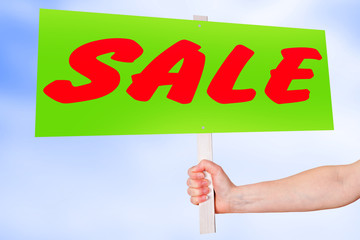 Hand holding sign with inscription SALE