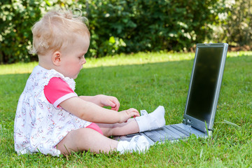 Baby sitting with laptop in a meadow