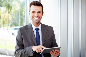 Happy businessman standing with laptop in office