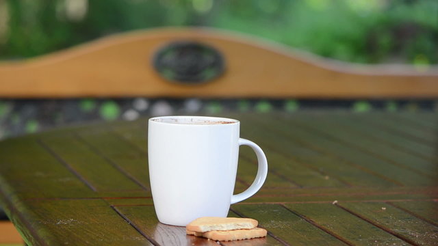 Steaming cup of hot coffee in white cup and few cookie biscuit