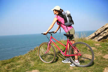 Fototapeta premium Young woman riding bike by ocean coast
