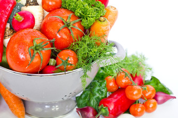 Fresh vegetables in metal colander over white