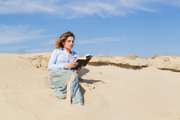 Attractive young blonde woman reading a book on the beach