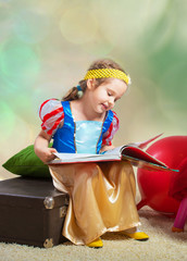 Smiling small girl sitting with a book and looking at pictures