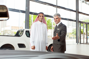 senior car salesman selling a car to arabic man