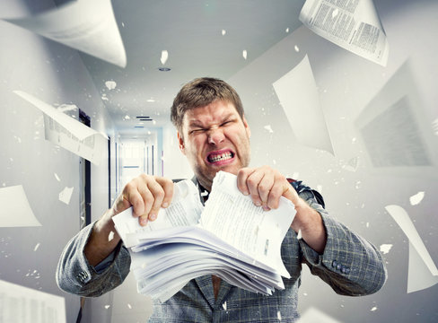 Stressed businessman tearing out stack of paper at office