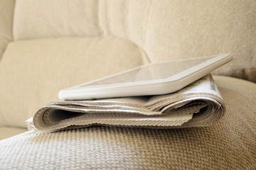 Tablet computer and newspaper on the couch
