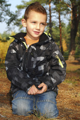 Boy sitting in autumn pine forest on earth.