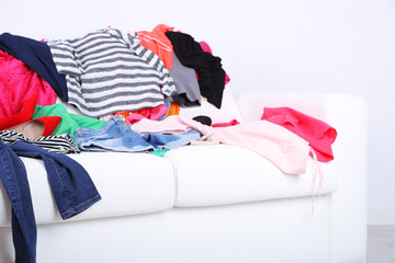 Messy colorful clothing on white sofa on white wall background