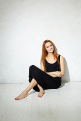 Skinny girl with long legs in black dress sitting on a white flo