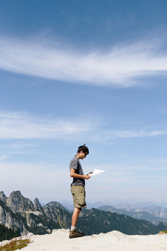 A hiker on the mountain summit, looking at a map. Surprise Mountain, Alpine Lakes Wilderness, in Mount Baker-Snoqualmie National Forest,