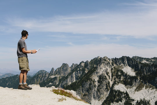 A hiker on the mountain summit, looking at a map. Surprise Mountain, Alpine Lakes Wilderness, in Mount Baker-Snoqualmie National Forest,