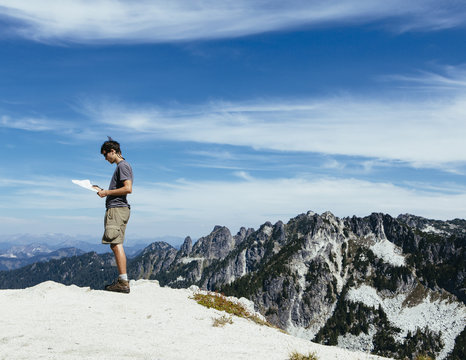 A hiker on the mountain summit, looking at a map. Surprise Mountain, Alpine Lakes Wilderness, in Mount Baker-Snoqualmie National Forest,