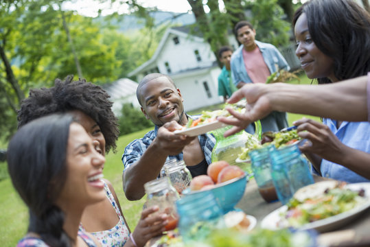 A group of adults and young people at a meal in the garden of a farmhouse.