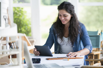 A woman working at a table, using a digital tablet. 