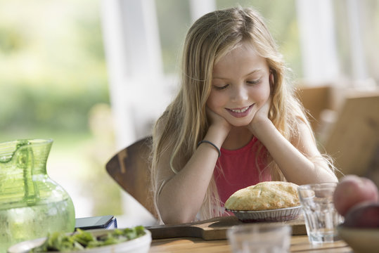 A young girl looking at a pastry pie, smiling. 